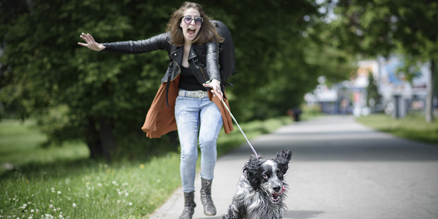 Young woman walking her dog on a street, having troubles holding him on a leash