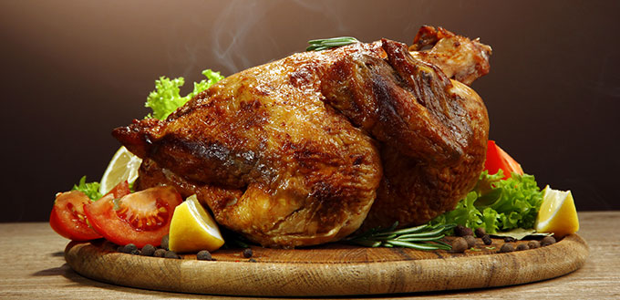 Whole roasted chicken with vegetables, on wooden table, on brown background