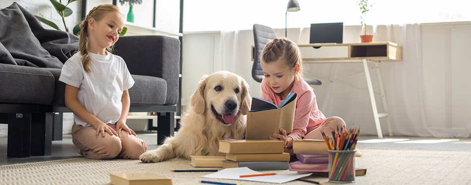 Little sisters reading books with golden retriever dog near by at home