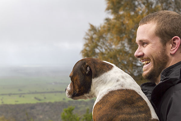 Solitary man aged 30, with his dog, outdoors with a stormy sky in the background