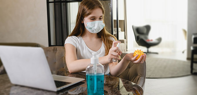 Young female stay at home during world epidemic quarantine, wear protective mask, use antiseptic for laptop, dog toy and hands