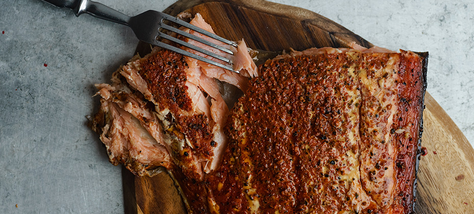 Smoked salmon with pepper on wooden cutting board on metallic surface