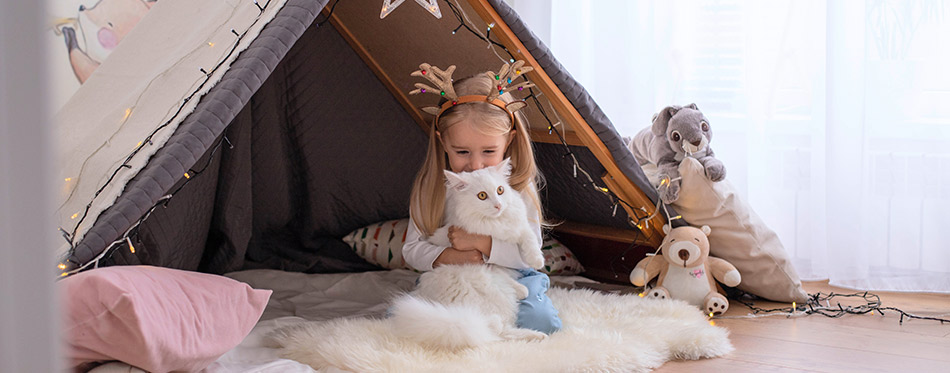 A little girl child is sitting in a children's room in a makeshift hut decorated with garlands with a white cat