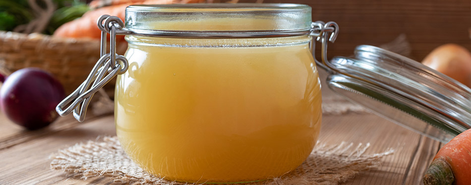 Chicken bone broth in a glass jar, with fresh vegetables in the background.