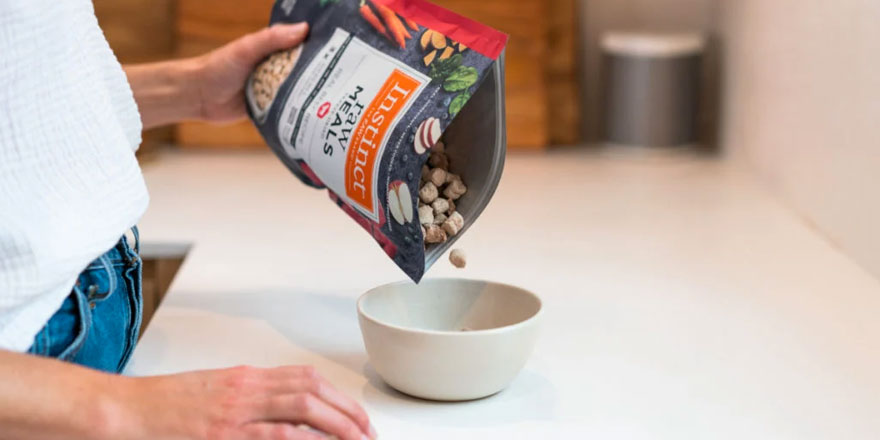 Woman in the kitchen is pouring frozen raw kibble into the dog bowl.