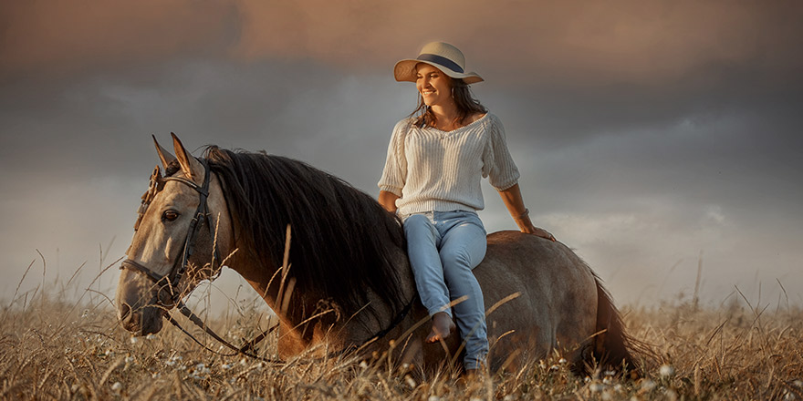 Beautiful young woman on spanish buckskin horse in rue field at sunset