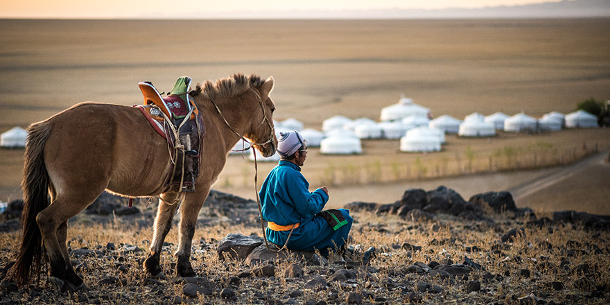 Mongolian Horse Rider In The Sunrise Morning By The Cliff Of The Mountain With Ger In Gobi Desert In Mongolia