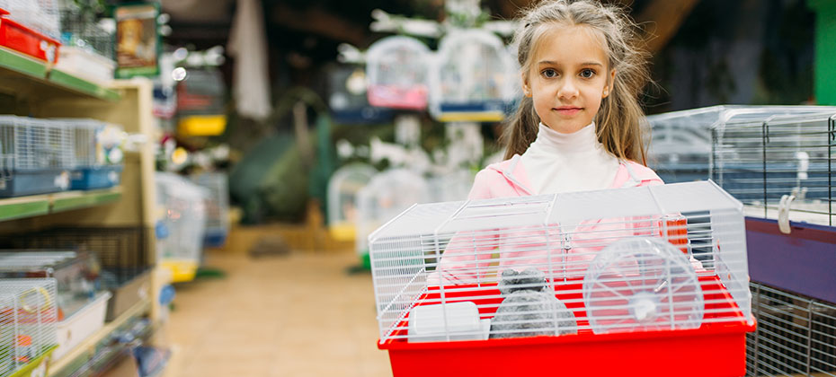 A little girl is holding a hamster cage in a pet shop