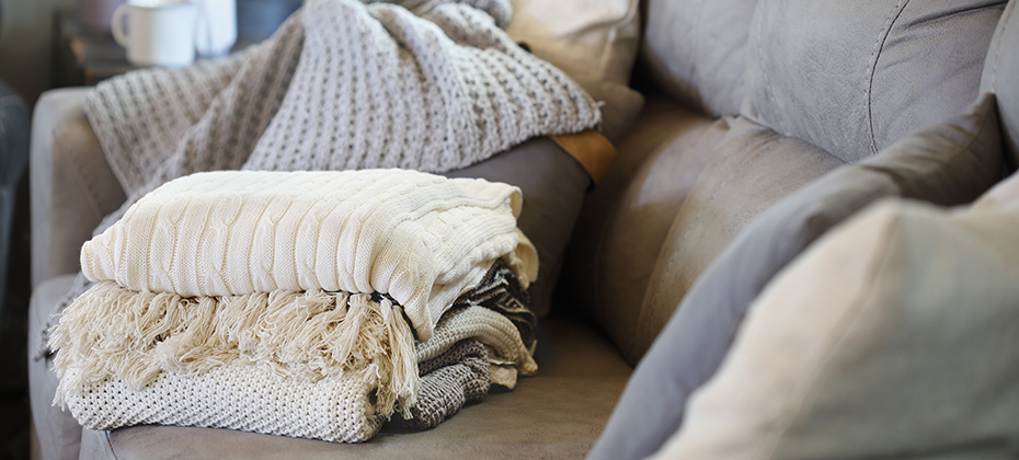 Stack of a variety of soft knit throw blankets stacked on a grey couch in a farmhouse style living room