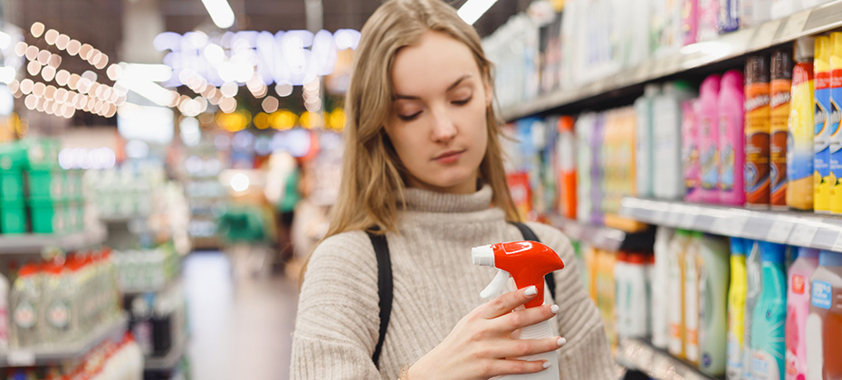 Young woman choosing spray for kitchen, bathroom at store